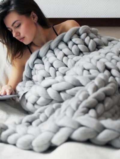On voit une femme dénudée dans son lit couverte d'une couverture en maille XXL grise.