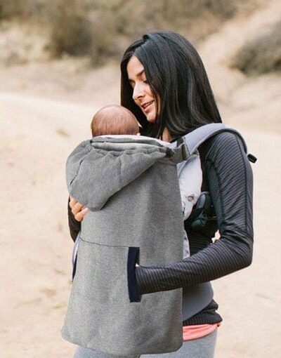 Femme portant son bébé dans un sac avec une couverture de portage. Fond naturel.