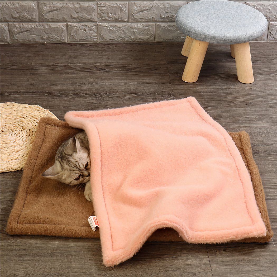 Au sol d'une pièce, on voit un chaton allongé sur une couverture marron et recouvert par une couverture rose. Il est prêt d'un tabouret.
