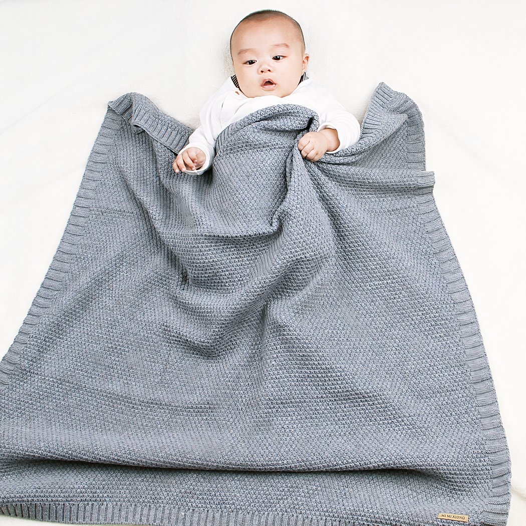 Bébé enveloppé dans une couverture tricoté en crochet de couleur grise.