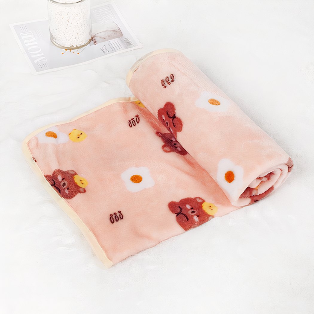 On voit une couverture rose ornée de motif oeuf sur le plat et ourson. Elle est en matière polaire et à demi roulée sur elle-même, sur fond blanc.