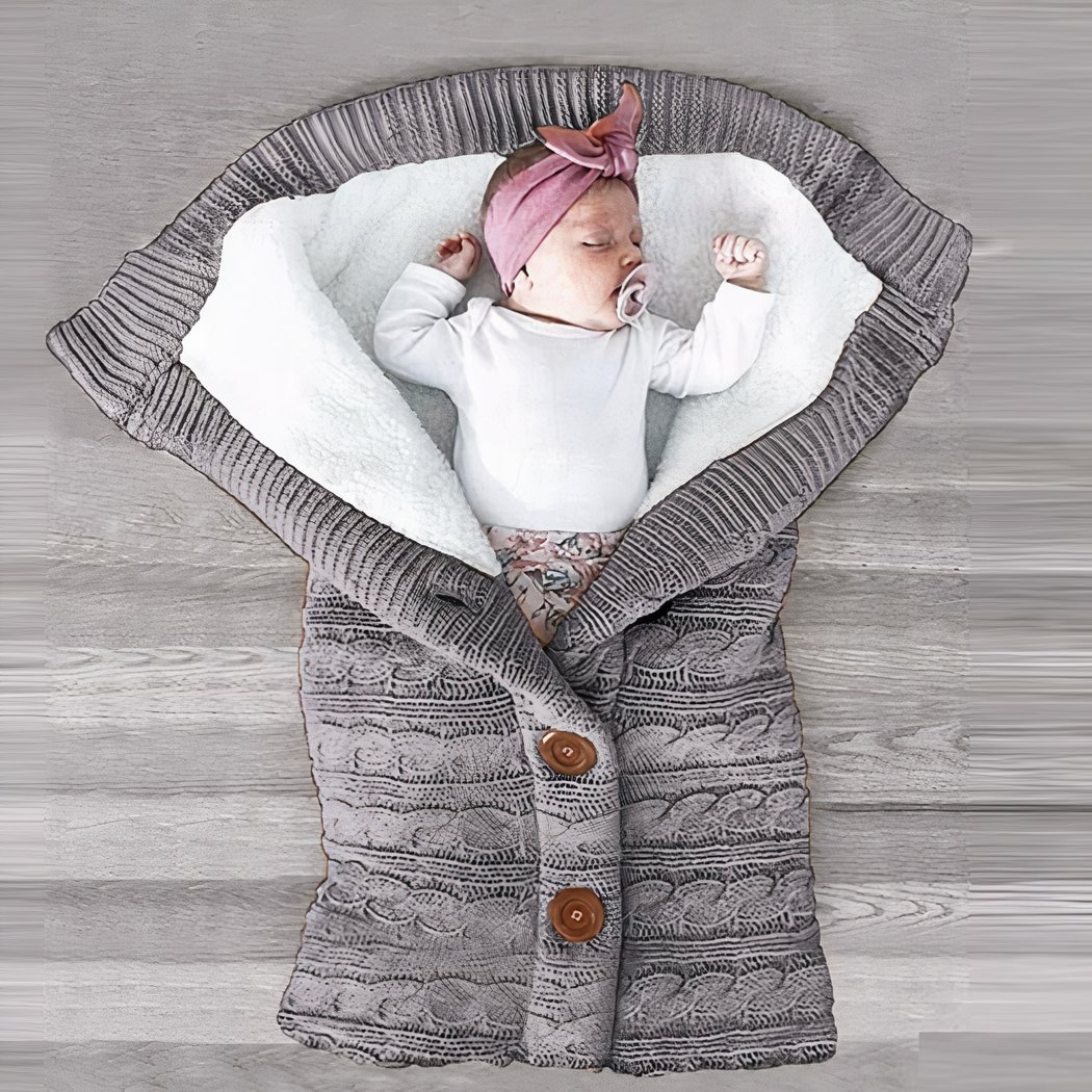Bébé enveloppé dans une couverture tricotée en crochet de couleur grise.