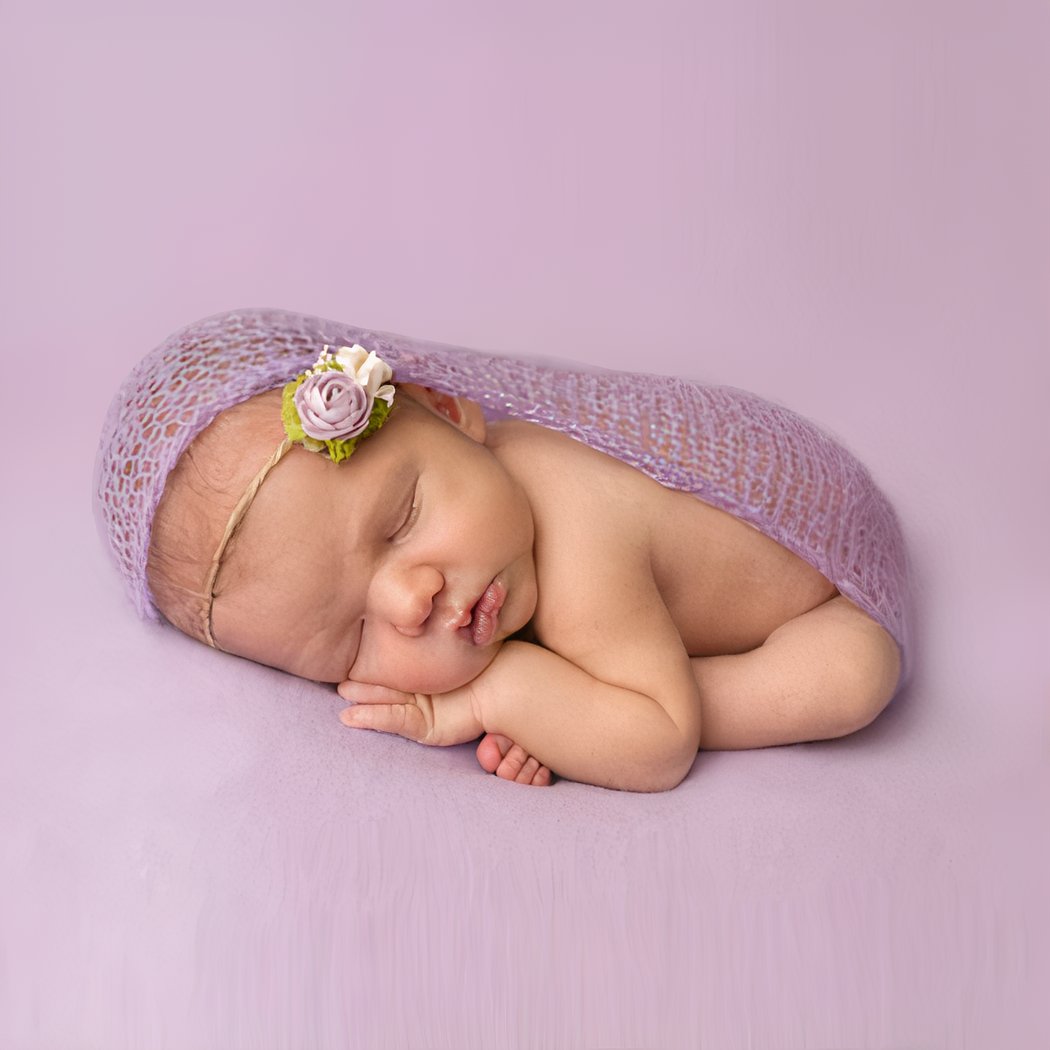 Bébé emmitoufler dans une couverture pour photographie avec un fond violet.