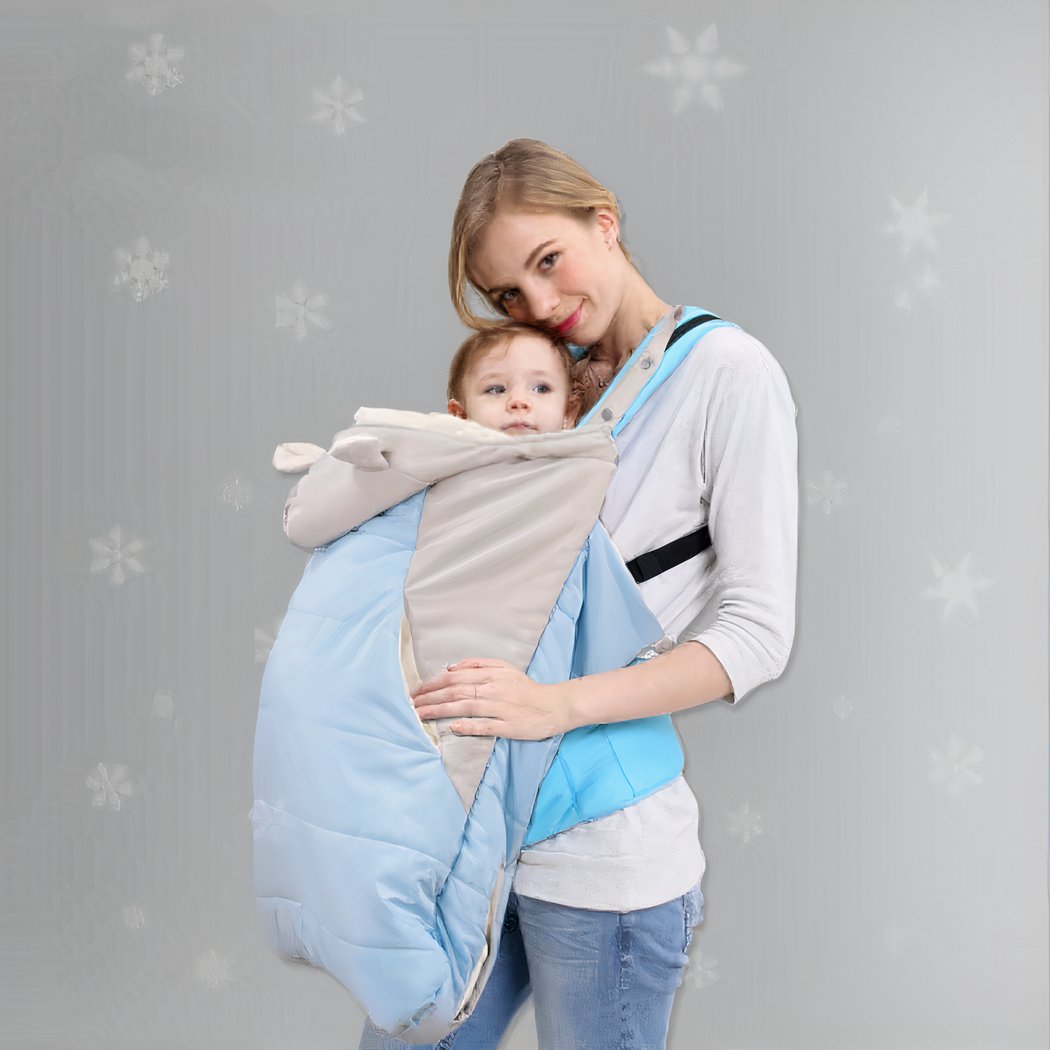 Femme portant un bébé dans une couverture de portage bleue, fond gris.