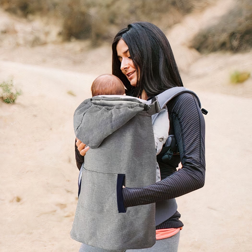 Femme portant son bébé dans un sac avec une couverture de portage. Fond naturel.