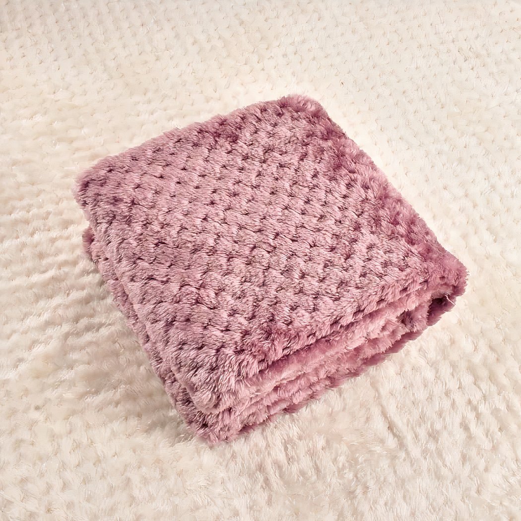 On voit une couverture rose foncé pliée en quatre sur une autre couverture beige étalée sur une surface plate. La couverture est épaisse.
