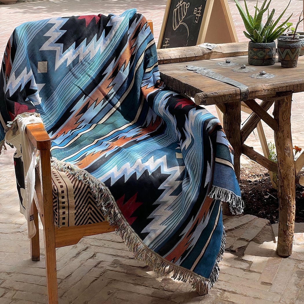 Photo d'une couverture mexicaine style ethnique bohème bleue posée sur une chaise à côté d'une table en bois