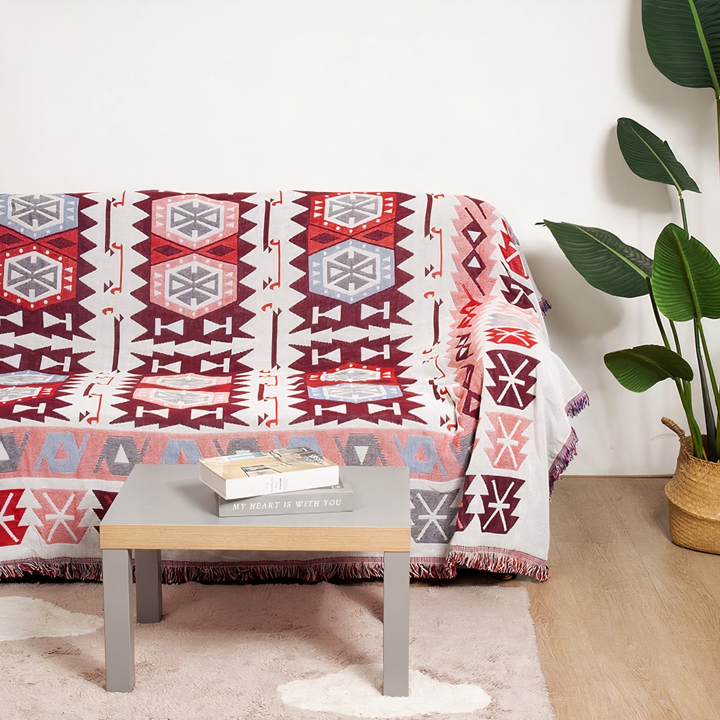 Photo d'une couverture mexicaine à motifs géométriques ethnique rouge et blanc posée sur un canapé devant une table basse à côté d'une plante.