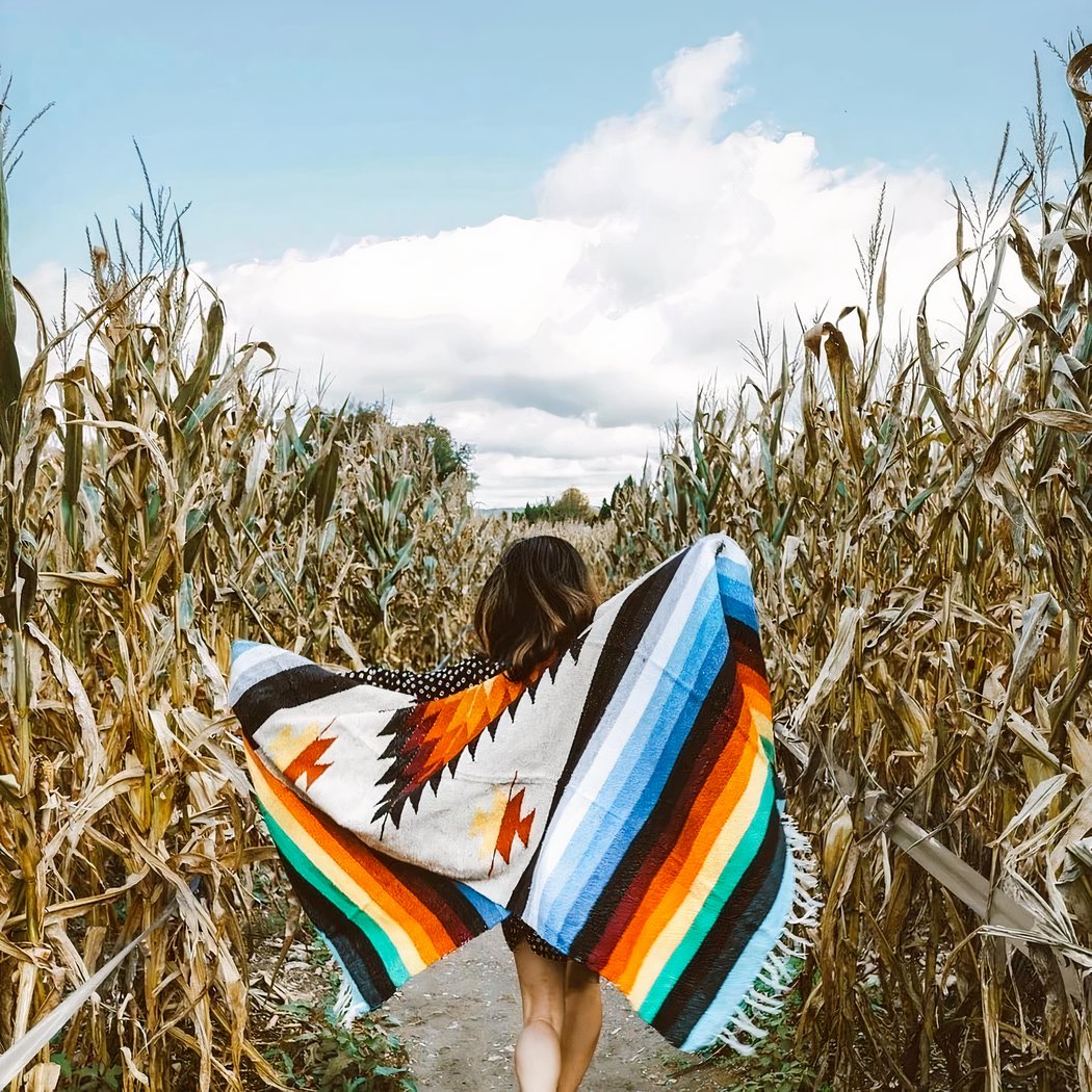 Photo d'une personne se baladant dans des champs de mais avec une couverture mexicaine colorée.