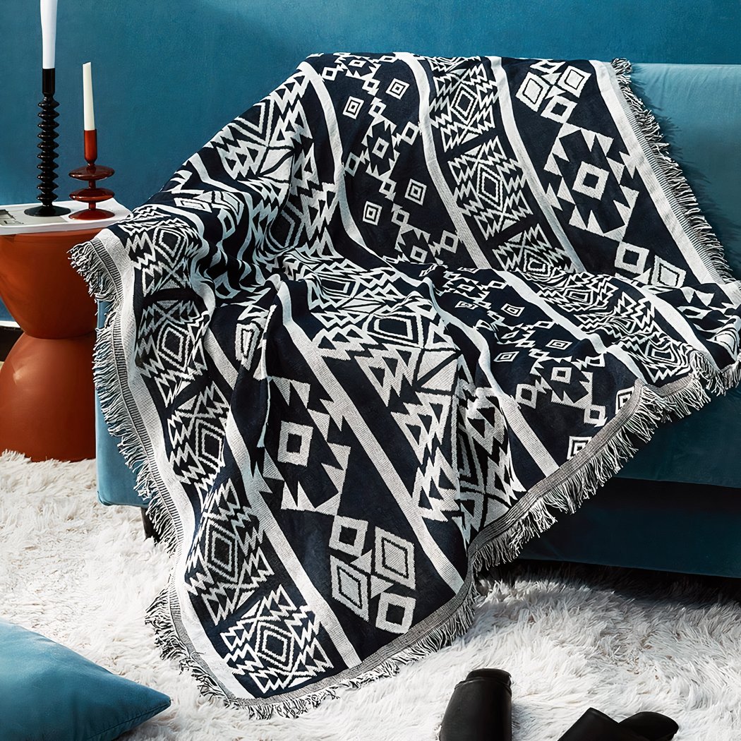 Photo d'une couverture mexicaine à motifs ethniques géométriques posée sur un canapé dans un salon avec un mur bleu canard à côté d'un meuble rouge et un tapis à poils blanc