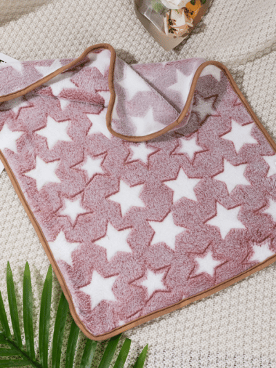 On voit une couverture rose pour chien assez grande. Il y a des motifs d'étoiles blanches dessus. Le contour est rose foncé. Elle est joliment présentée comme sur un magazine de décoration.