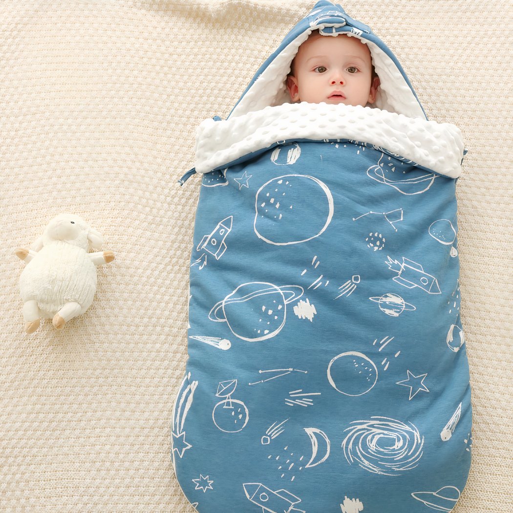 Enfant allongé sur un tissu beige dans une couverture à capuche bleue avec son doudou blanc à côté de lui
