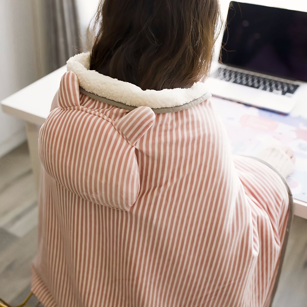 Femme assise devant un ordinateur portable portant une couverture rose à rayure avec un coussin dessus.