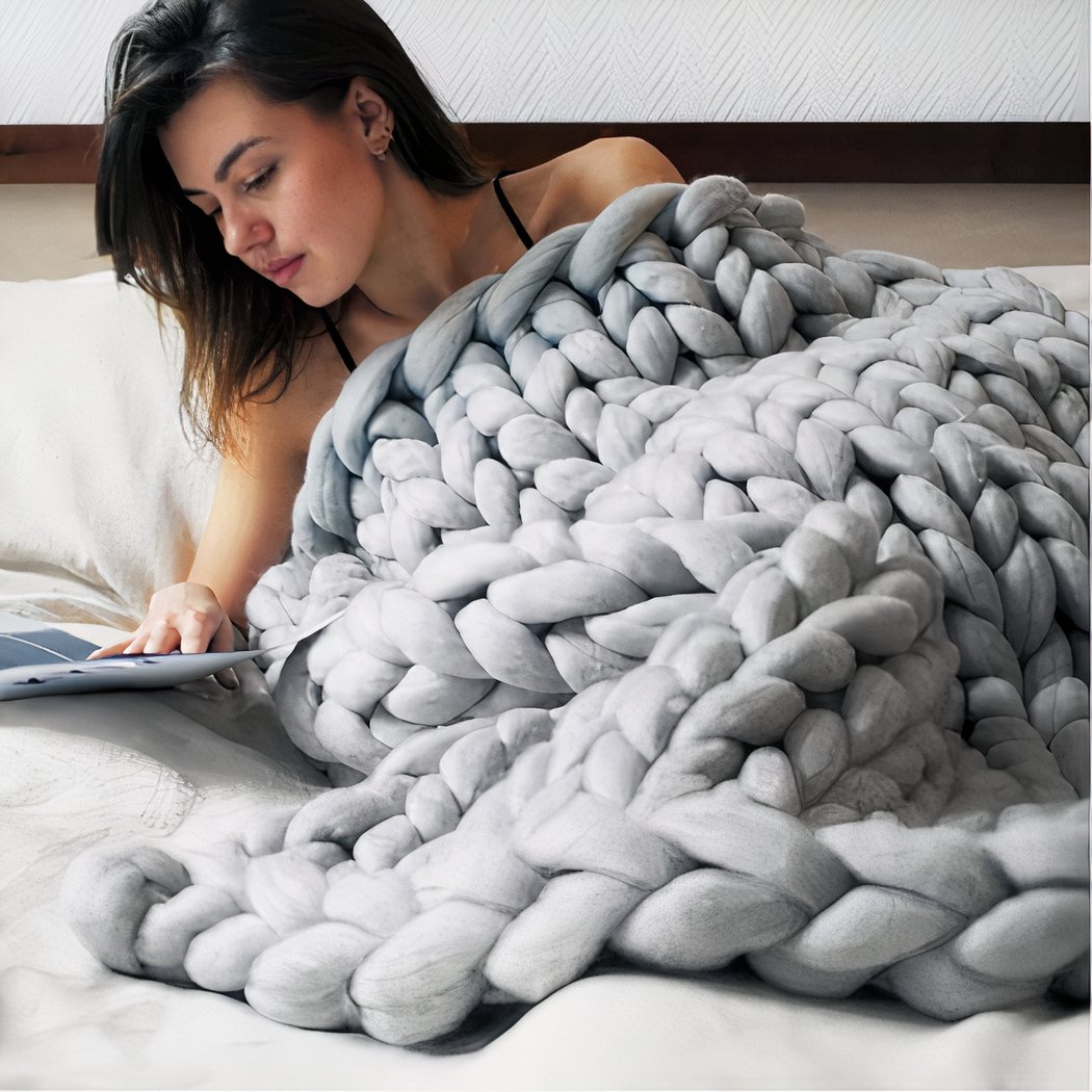 On voit une femme dénudée dans son lit couverte d'une couverture en maille XXL grise.