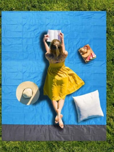 Couverture pique-nique de couleur bleu entendue sur l'herbe avec une femme lisant un livre allongée dessus