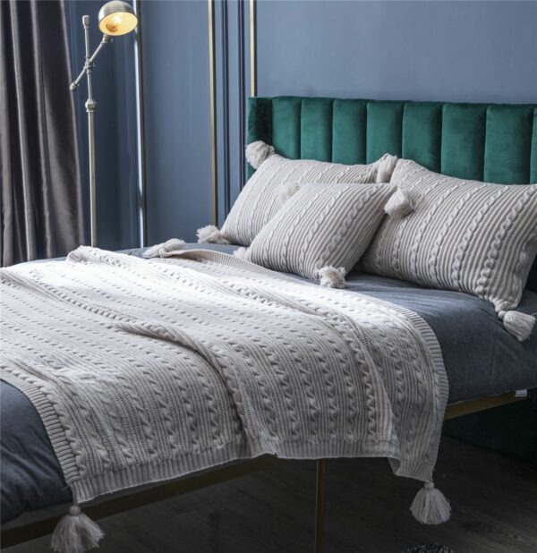Dans une chambre il y a un lit double avec une couverture grise et trois oreillers gris posés dessus.
