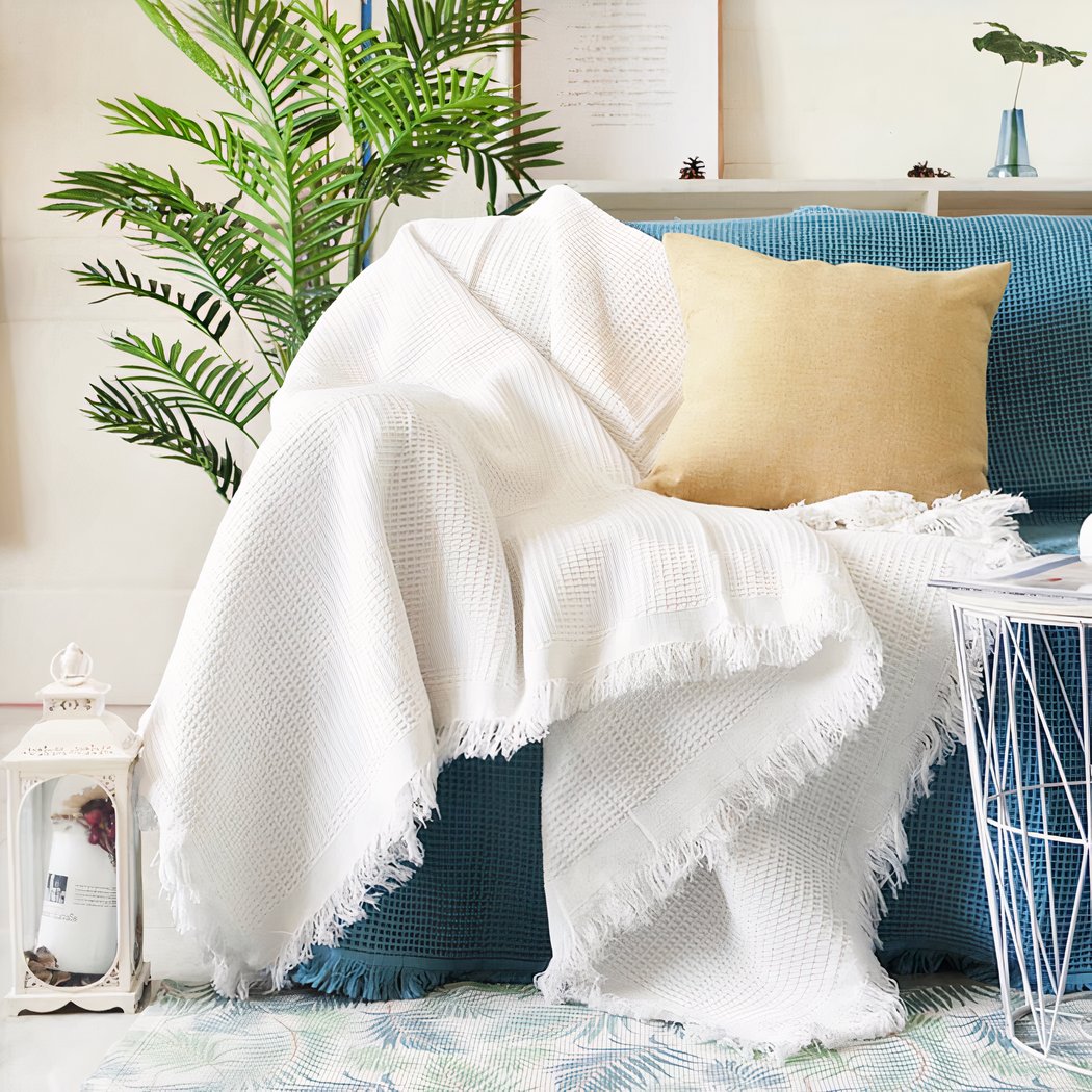 On voit la moitié d'un canapé dans un salon. le canapé est bleu recouvert d'une couverture blanche et d'un coussin jaune.