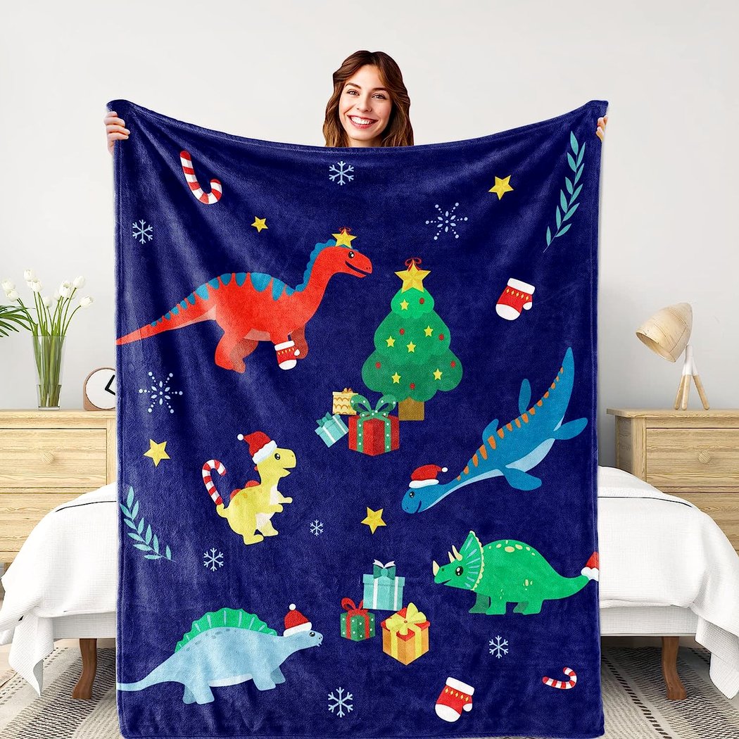 Mannequin femme dans une chambre à coucher, devant un lit 2 places, tenant devant elle un plaid bleu avec des dessins de dinosaures et de Noël. On ne voit que la tête de la mannequin brune et les mains qui tiennent le plaid.