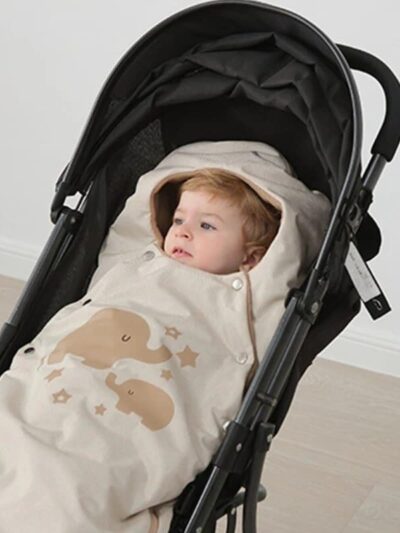 Couverture Poussette Beige et Mignonne pour Bébé sur une poussette noire avec un bébé sur fond beige